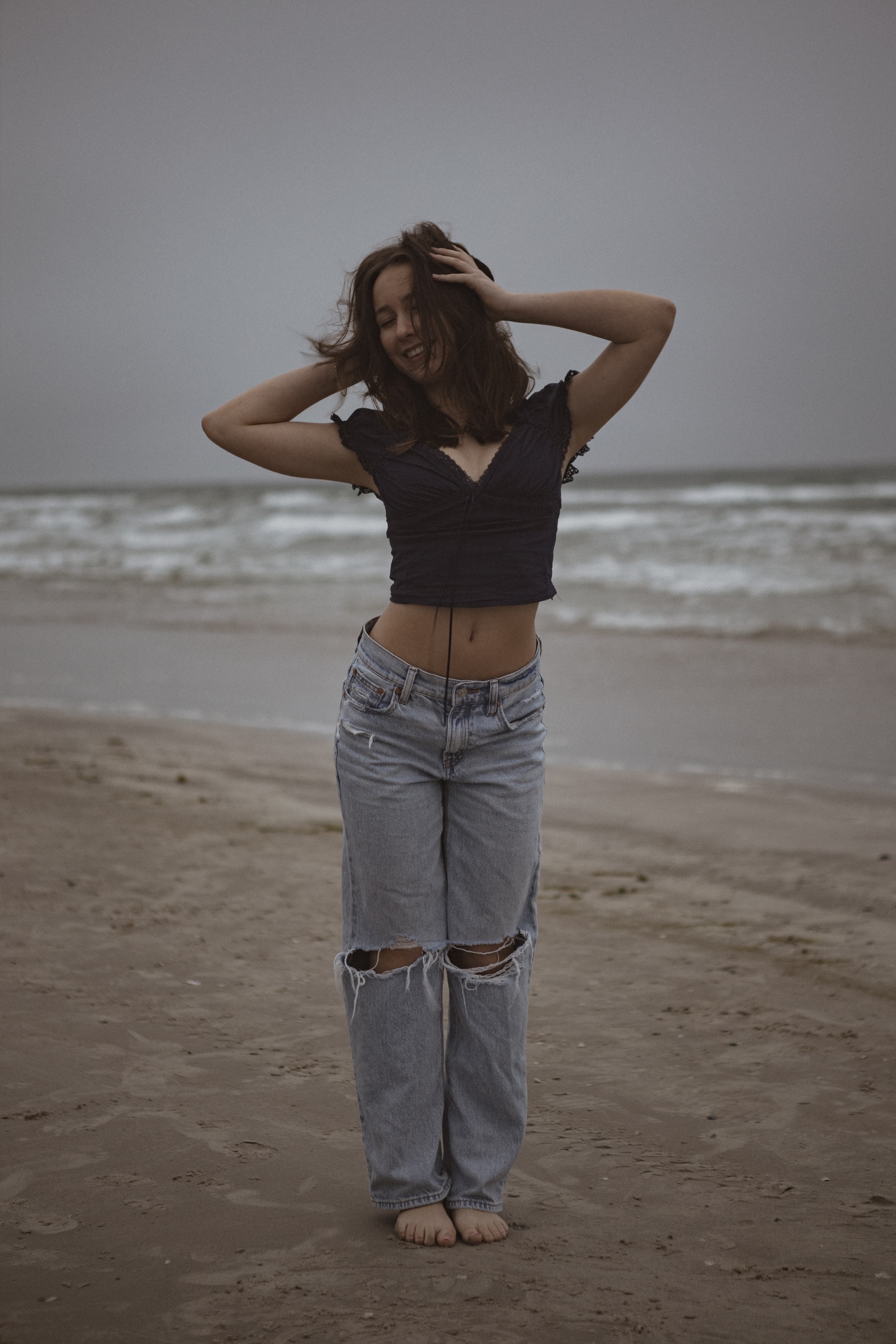 Full-length portrait on the beach beneath an overcast sky